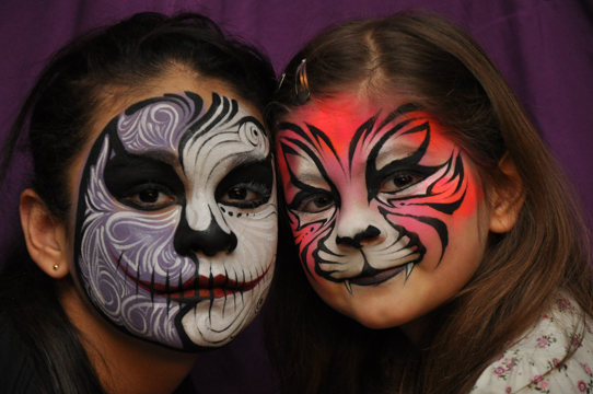 two girls in a full face paint one with a skull theme and the other in a pink tiger theme